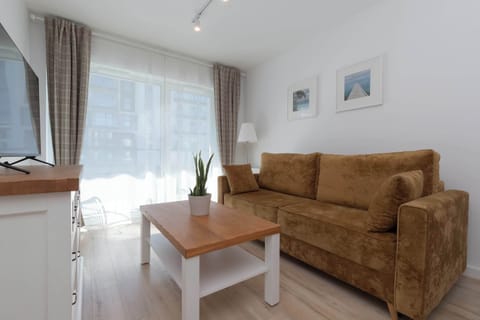 A cozy living area with a brown sofa, white coffee table, and large window with sheer curtains.
