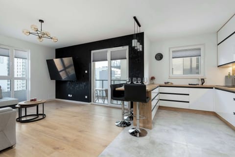 A wide-angle view of the open-plan living room and kitchen. The modern interior design features a combination of white and black elements with wooden accents.
