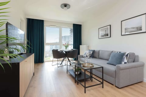 A bright living room featuring a large gray sectional sofa, a modern coffee table, and a TV cabinet with a flat-screen TV.