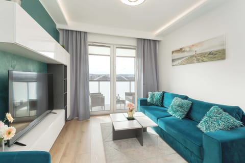 A bright living space features a teal sofa, a patterned rug, and a large window.