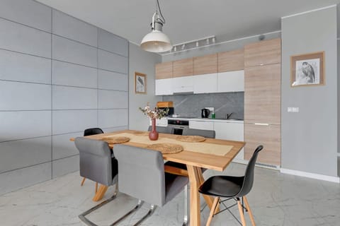 A modern kitchen open to the living room combines functionality with aesthetics. Furniture in shades of white and light wood harmoniously complements the marble floor, creating a space full of class and order.