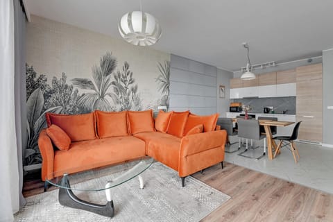 A vibrant living area featuring an orange sectional sofa, a stylish wall mural, and modern decor.