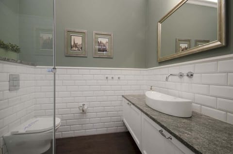 The large shower cabin with transparent doors is the focal point of this interior. Above the gray countertop, there's a stylish mirror in a golden frame, which visually enlarges the space.
