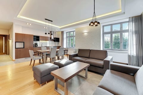 A contemporary living space with a gray sectional sofa, a flat-screen TV, and views of greenery through the windows.