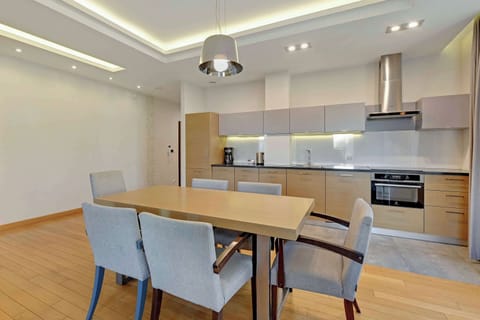 A spacious dining setup with a wooden table and upholstered chairs, surrounded by natural light from large windows.