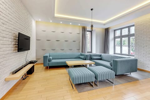 A modern living room with a sectional sofa, a flat-screen TV, and warm wooden floors complemented by soft lighting.