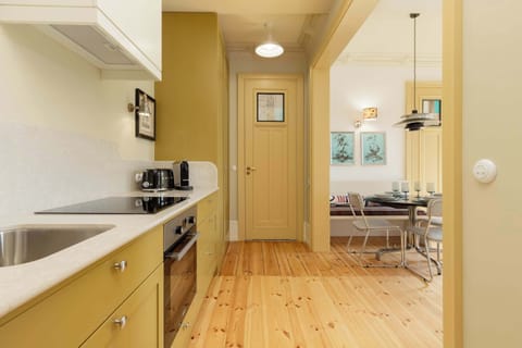 A compact kitchen with light yellow cabinetry, a stove, oven, and a window in the background.