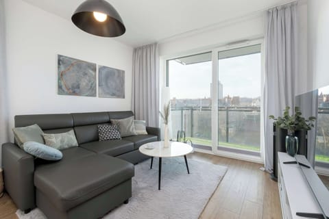 A spacious living room with a comfortable gray sectional sofa, a coffee table, and floor-to-ceiling windows leading to a balcony.