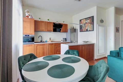 A modern kitchen with wooden cabinets, an oven, and a dining area with a round glass table and chairs.