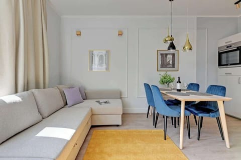 A living room with large windows, light-colored furniture, and plants, creating a cozy atmosphere.