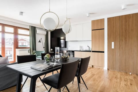 This dining area features a round black dining table with modern, minimalistic chairs. The large window behind offers a view, and a simple, elegant light fixture hangs above.