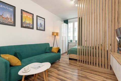 The cosy living area with a green sofa with a coffee table is separated from the bedroom area by wooden panels.
