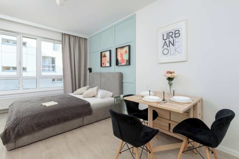 The main living area features a cozy bed, a small dining table for two, and large windows that let in plenty of natural light, creating a bright and airy atmosphere.