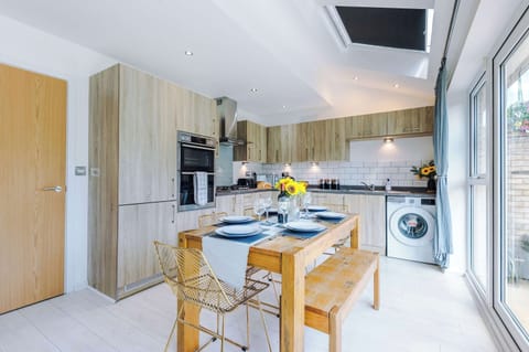 Bright, modern kitchen with full appliances, stylish wood cabinetry, and a spacious dining area. Enjoy meals at the rustic table with views of the garden through large French doors. Perfect for cooking, dining, and gathering.