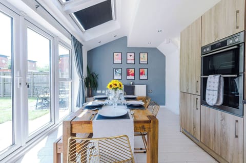 Bright, modern kitchen with full appliances, stylish wood cabinetry, and a spacious dining area. Enjoy meals at the rustic table with views of the garden through large French doors. Perfect for cooking, dining, and gathering.