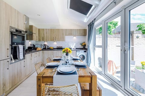 Bright, modern kitchen with full appliances, stylish wood cabinetry, and a spacious dining area. Enjoy meals at the rustic table with views of the garden through large French doors. Perfect for cooking, dining, and gathering.