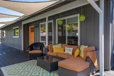 Welcome home to this modern, inviting retreat! The covered patio features sleek grey siding and an eye-catching orange door. Enjoy the relaxed atmosphere of the plush outdoor seating, anchored by a green geometric rug. 
