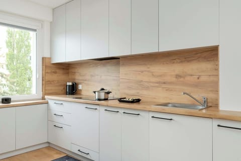 The modern kitchenette with white cabinets, a wooden backsplash, and sleek appliances creates a functional and stylish space for meal preparation.
