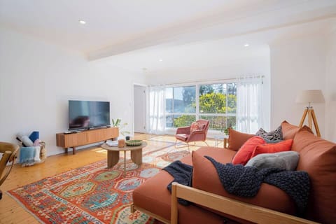 Step into a calm lounge where natural light streams through oversized windows, framing leafy views and soft glimpses of Woy Woy Bay—a perfect place to unwind after an active day.