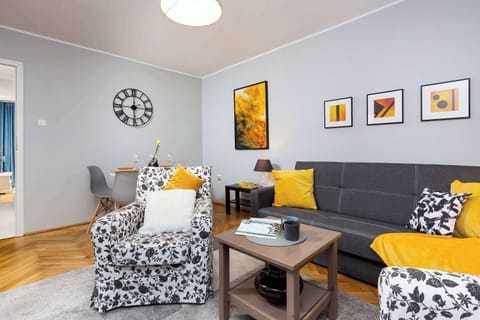 A cosy living room with a grey sofa bed over which pictures hang. A comfortable two armchairs in floral accents add to the charm of the room.