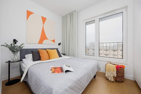 A bedroom with a large bed, orange wall art, and a bright, airy atmosphere.