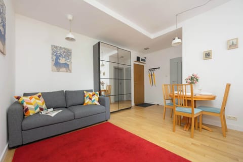 A cozy living and dining area with a gray sofa, wooden furniture, and a red rug on a light wood floor.