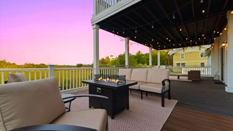 Sip wine by the fire table and take in serene marsh views from this dreamy covered deck. With cozy cushioned seating, string lights overhead, and the soft glow of sunset, this outdoor space is