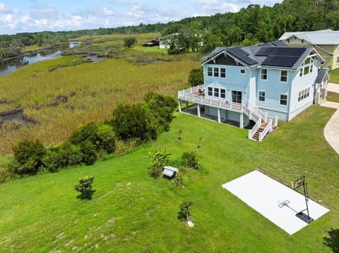 Three-story home with solar panels, two decks, and a spacious backyard featuring a basketball court, surrounded by a scenic marshland view
