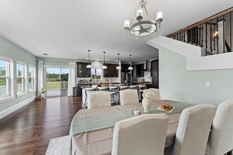 Spacious open-concept dining and kitchen area, perfect for gatherings. Features elegant hardwood floors, modern lighting, and ample natural light from large windows and patio doors leading to the outdoor deck