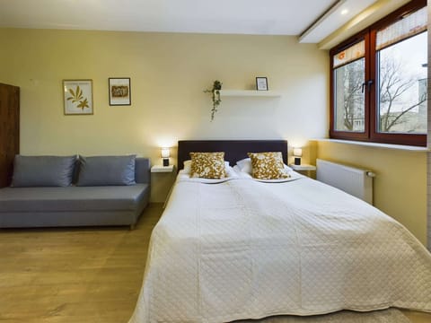 A compact and inviting sleeping area with a double bed and gray sofa, stylish bedding, and soft lighting for a relaxing atmosphere.