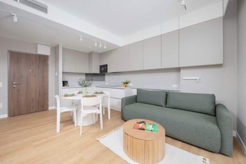 A bright and stylish living room with a comfortable green sofa and a small dining table for four.