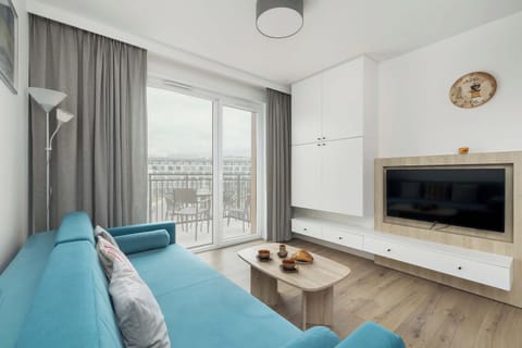 The spacious living room impresses with a comfortable blue sofa, a large TV hanging on the wall and light, delicate curtains that let in plenty of natural light, creating a cozy atmosphere.