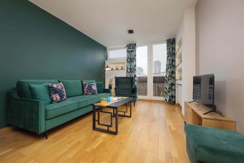 A cozy living room featuring a deep green sofa and a wooden coffee table. The room is decorated with neutral tones and has a comfortable ambiance.