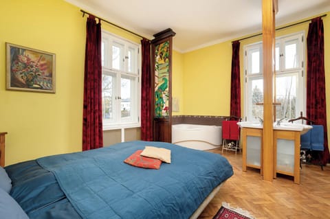 A bright and spacious bedroom, where a large bed, warm yellow walls and two windows with red curtains create a cozy atmosphere.