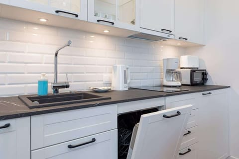 A kitchen equipped with a stove, sink, and sleek white cabinetry, designed for convenience.