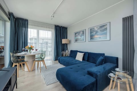 A cozy living room with a blue sofa, a coffee table, and stylish decor. Large windows let in plenty of natural light.