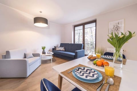 A cozy living room with a modern blue and gray sofa, a round coffee table, and a window letting in natural light. A small vase with flowers adds charm.