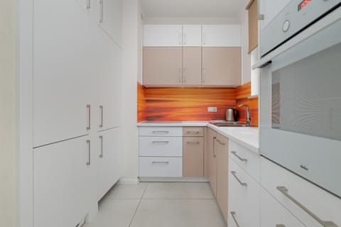 A fully equipped kitchen with white cabinetry, an orange backsplash, and built-in appliances, combining functionality with a pop of color.


