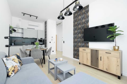 Bright, apartment decorated in shades of gray, white, with additions of wood and black. There is a TV on the wall, a wooden chest of drawers stands underneath.