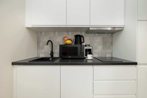 A compact kitchen with sleek white cabinets and a black granite countertop. Equipped with modern appliances, including a coffee maker and microwave.