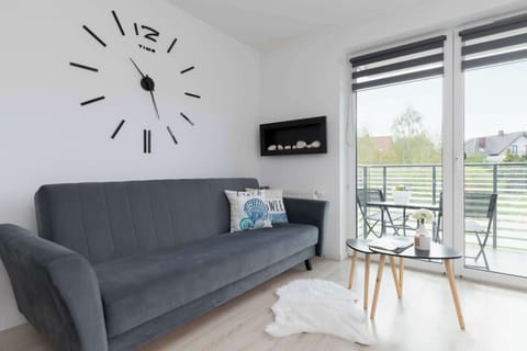 A bright room, with a graphite sofa with decorative pillows, with a small coffee table, and a decorative clock on the wall.