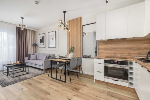 A living room scene highlighting the wooden accent wall where a flat-screen TV is mounted. The gray sofa faces a black coffee table, and floor-length curtains frame the window.

