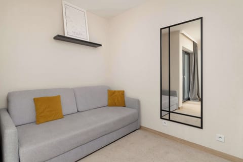 A bright living space with a modern gray sofa, yellow accent pillows, a minimalist shelf, and a large mirror.