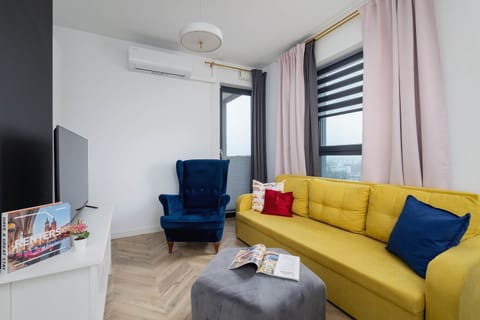 A bright, air-conditioned living room with a mustard-coloured sofa and a navy blue armchair standing next to it.