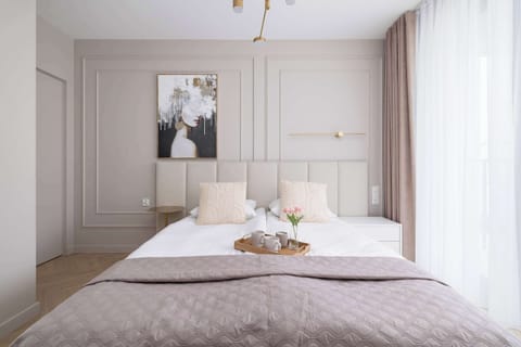A cozy bedroom with a large double bed, elegant wall molding, and sheer curtains filtering natural light.

