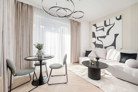 A stylish living room with a modern chandelier, a beige couch, a round black coffee table, and a large window with curtains.