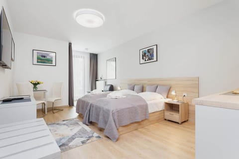 A spacious bedroom with a double bed, light wood furniture, and a soft color scheme. The large window brings in ample natural light, creating an airy atmosphere.