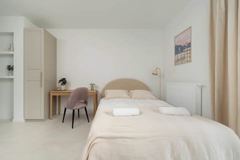 A bright studio with a bed, wardrobe, and small desk in a cozy arrangement.