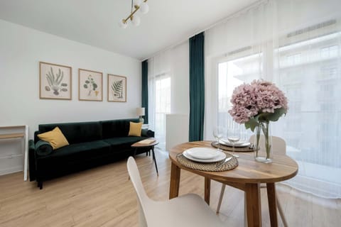 A bright living area with a green sofa, a round coffee table with a vase of pink flowers, and framed wall art.