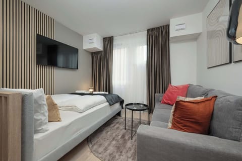 A cozy living area with a grey sofa, vibrant orange accent pillows, and a wall-mounted TV, creating a modern and comfortable space.

